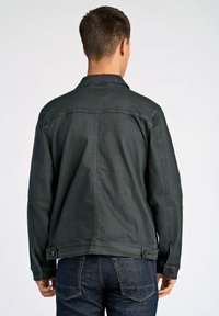 Chaqueta de denim verde oscuro con un cuello tipo solapa, acentos de botones en los puños y un corte recto. Lleva puesta con vaqueros azul.