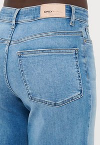 Svetle modré džíny s rovnýcm střihem, obsahující zadní kapsu a koženou štítek na pase s nápisem "ONLY Plus Denim."