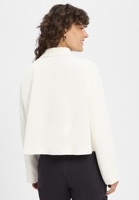 Witte cropped blazer met een gladde textuur, voorzien van een reverskraag en lange mouwen, gezien vanaf de achterkant.
