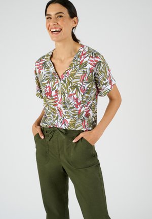 Blusa a maniche corte con stampa floreale tropicale in verde, rosa e bianco. Abbinata a pantaloni verde oliva con vita regolabile e tasche.