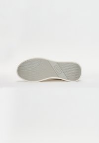 Fehér sneaker talp, jól tapadó textúrával, formázott gumi szerkezettel és középen elhelyezett logóval.