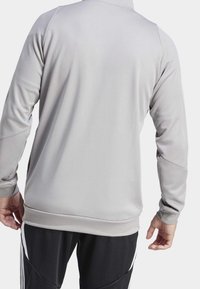 Hellgrau sportliche Jacke aus glattem Stoff, mit langen Ärmeln und einem dezenten Rundhalsausschnitt. Keine sichtbaren Logos oder weiteren Details.