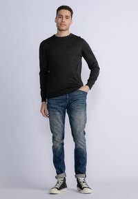Dark gray long-sleeve knitted sweater paired with light blue, slightly faded jeans and black high-top sneakers with white soles.