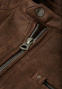 Giacca in finta pelle marrone con una zip argentata, chiusura a scatto in metallo e superficie texture. Caratterizzata da cuciture evidenti e colletto alto.