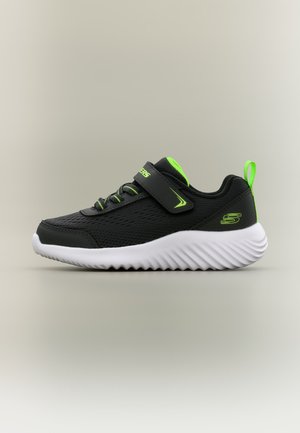 Baskets sportives noires et vert néon avec semelle blanche ondulée, lacets élastiques et une bride velcro affichant le logo Skechers sur le côté.