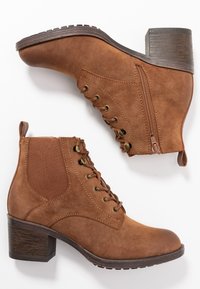 Bottines en daim brun avec un talon empilé, présentant un devant lacé, une fermeture éclair sur le côté et un panneau en élastique texturé pour un ajustement parfait.
