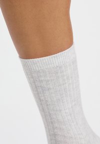 Calcetín de tobillo de color gris claro, acanalado y hecho de un material suave, con un borde superior doblado y una textura sutil. Adecuado para uso casual.