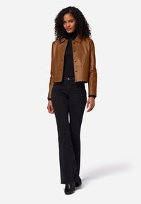 Bruine leren cropped jack met een kraag, knoopsluiting aan de voorkant, gecombineerd met zwarte flared jeans en zwarte laarzen met hak. Gladde textuur.