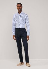 Camisa de manga larga a rayas blancas y azules con cuello abotonado, combinada con pantalones azul marino y zapatos de cáñamo de color beige claro.