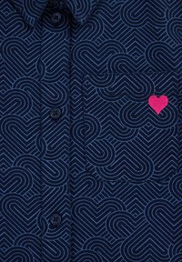 Maglietta navy con un motivo di cuori a spirale in blu chiaro, con un cuore ricamato rosa sulla tasca e bottoni neri.