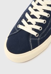 Μπλε ναυτικό πάνινο παπούτσι απ�ό κορντόνι με κρεμ κορδόνια και ραφές, με υφασμένο πάνω μέρος και μπεζ λαστιχένια σόλα για καλύτερη πρόσφυση.