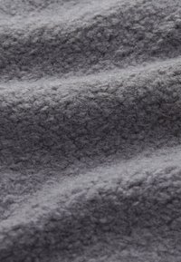Tissu gris avec une surface texturée, mettant en valeur des fibres douces et surélevées ainsi que des ondulations, évoquant chaleur et confort.
