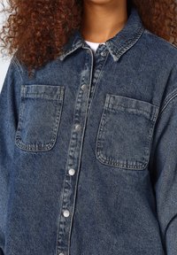 Camicia in denim blu scuro con design a bottoni, due tasche sul petto, colletto e un finish testurizzato.
