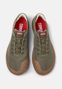 Green fabric sneakers with a rubber brown sole, rounded shape, and lace-up design. Features a red "CAMPER" logo on the tongue.