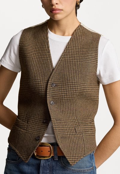 Gilet marron à motif pied-de-poule avec un col en V, doté de deux boutons et de poches latérales, porté sur un T-shirt blanc, associé à une ceinture marron.