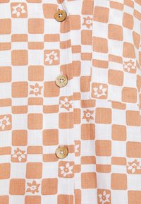 White fabric shirt featuring an orange checkered pattern with floral accents. Notable details include wooden buttons and a lightweight texture.