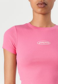 Figurbetontes, geripptes pinkes T-Shirt mit kurzen Ärmeln und Rundhalsausschnitt. Mit einem kleinen weißen "guess jeans"-Logo auf der Brust.