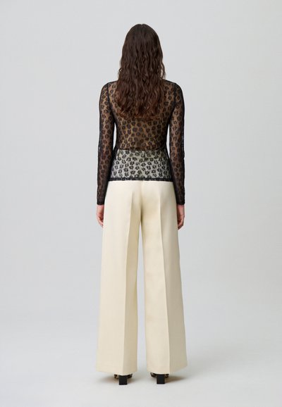 Top in pizzo nero a maniche lunghe con motivi floreali, abbinato a pantaloni larghi color crema con texture liscia e vestibilità comoda.
