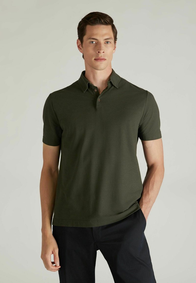 Polo de manga corta verde oscuro con cuello, que cuenta con tres botones y una tela texturizada. Combinado con pantalones oscuros.