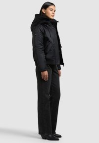 Jachetă neagră cu puf și glugă, cu manșete elastice și fermoar frontal. Asortată cu blugi negri cu talie înaltă și picioare largi, precum și cizme negre cu toc.