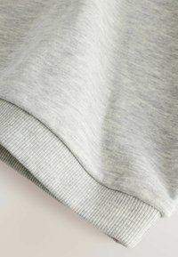Harmaa collegehupu, jossa on sileä pinta ja ribbaushelma. Materiaalissa on hienovarainen heather-kuvio, joka luo visuaalista kiinnostavuutta.