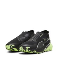 Fekete sportcipők, slip-on kialakítással, textúrált zöld és fekete katonai mintázatú talppal és oldalsó betétekkel a tapadás érdekében.