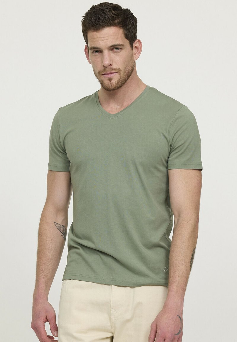 T-shirt vert à col en V fabriqué en coton doux, design ajusté, manches courtes, avec un petit logo près de l'ourlet.