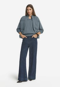 Hellblaue Strickjacke mit strukturiertem Design, kombiniert mit einem passenden Strickpullover und dunkelblauen weiten Jeans. Schwarze spitze Schuhe und Armband.