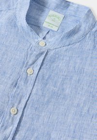 Světle modré a bílé pruhované polo tričko, slim fit, zapínání na knoflík, měkká tkanina a štítek zobrazující informace o značce a velikosti.