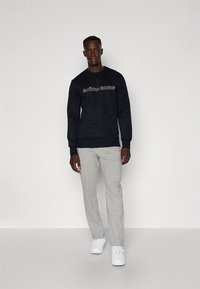 Sweatshirt azul-marinho com o texto "BJÖRN BORG", combinada com calças de fato de treino cinza claro e ténis brancos. O conjunto apresenta um corte descontraído e um design casual.