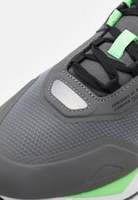 Gray athletic shoe with textured fabric, green accents, reflective silver detail, and black laces. Rubber sole with cushioning for comfort.