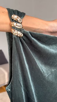 Tumši zaļš samta apģērbs, kas uzlikts uz rokas, ar trim spīdīgām zelta aksesuāriem, kas nostiprina audumu pie pleca.