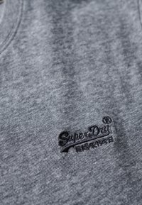 Grijs gebreid T-shirt met een ronde hals en een textuurafwerking. Geborduurd "SuperDry" logo in de onderste linkerhoek.
