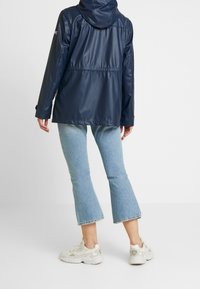 Merihenkinen vedenkestävä takki hupulla, joustavalla vyötäröllä ja pitkät hihat. Yhdistetty vaaleansinisiin leveälahkeisiin farkkuihin ja valkoisiin tennareihin.