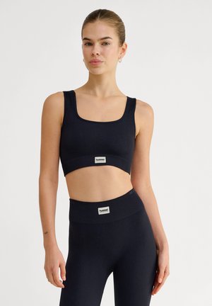 Donkerblauwe geribbelde sportbeha met een vierkante halslijn en brede banden. Bevat een logopatch bij de zoom. Gecombineerd met bijpassende geribbelde leggings.