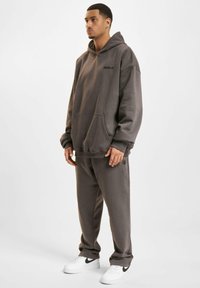 Gray hoodie with a front pocket and logo, paired with matching gray sweatpants, worn with white Nike sneakers. Soft, textured fabric.