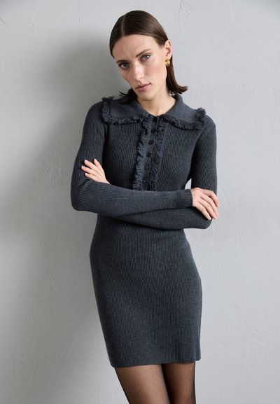 Gray ribbed sweater dress with a frayed collar, button closure, and long sleeves, paired with black stockings. Smooth texture, fitted silhouette.