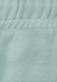 Helle tealfarbene Stoff mit glatter Textur und geripptem Taillenbanddetail. Das Material wirkt weich und leicht dehnbar, geeignet für Freizeitbekleidung.