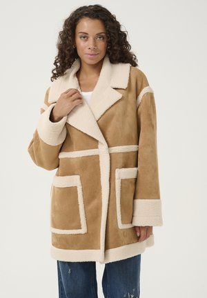 Brown suede coat with cream shearling accents, large patch pockets, and a wide lapel collar; features a relaxed fit and textured fabric.