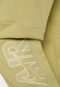 Olive green hoodie featuring prominent white "AIR" logo with textured accents, made from soft, stretchy fabric. Clean seams and cuffs.