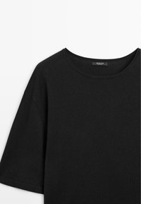 T-shirt noir à manches courtes avec col rond et étiquette de marque visible à l'intérieur du col, posé à plat sur un fond blanc.