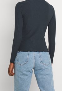 Top nero a maniche lunghe rigato con design aderente, orlo smerlato, abbinato a jeans in denim azzurro chiaro a vita alta con tasche posteriori.