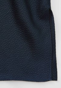 Dunkelblauer Stoff mit einer strukturierten Oberfläche, die ein wellenförmiges, gemustertes Design aufweist. Der Stoff hat einen leichten Glanz und Seitenschlitze.