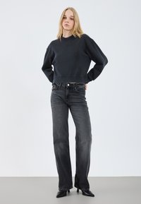 Felpa nera corta con colletto a girocollo e spalle scese, abbinata a jeans svasati grigi scuri e scarpe con tacco nere.