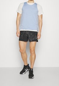Light blue athletic tank top over a white base layer, paired with black patterned shorts. Black sneakers with white accents.