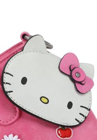 Portafoglio in peluche rosa con design Hello Kitty, caratterizzato da un viso bianco ricamato, dettagli neri e un fiocco rosa. Include una ciliegia ricamata.