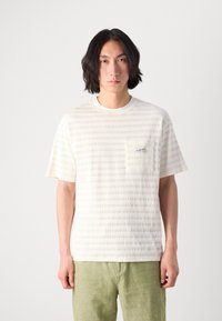Hvid kortærmet T-shirt med teksturerede striber, har en brystlomme med et logo-tag, parret med lysegrønne shorts.