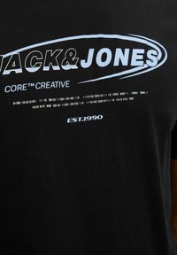 Mustatyön t-paita, jossa on "JACK & JONES" valkoisena ja vaaleansinisellä sekä binäärikoodikuosi, jonka alla lukee "EST.1990".