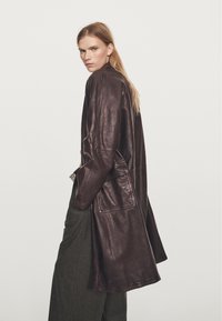 Bruine leren jas met een relaxte pasvorm, lange mouwen, zijzakken en een gladde, soepele textuur. Heeft een ontwerp tot halverwege de dij.