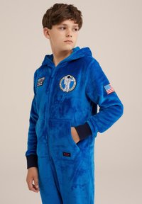 Zils frotēts kombinezons ar rāvējslēdzēju, kapuci un ribinātām piedurknēm, kurā ir astronauta noformējums un uz kabatas ir uzraksts "ES NEGUĻU".